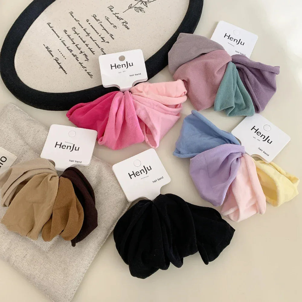 Various sets of scrunchies in different color palettes displayed on a light-colored surface, with decorative elements in the background.