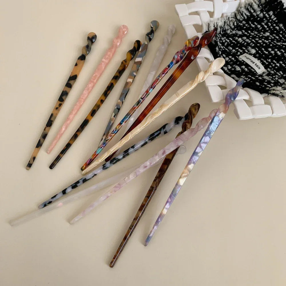 Several patterned hair sticks arranged on a light-colored surface with a textured fabric item.