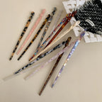 Several patterned hair sticks arranged on a light-colored surface with a textured fabric item.