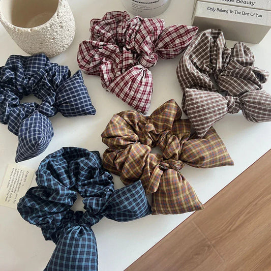 Collection of plaid scrunchies with bow details in various colors including navy, burgundy, brown, and tan.
