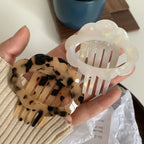 A hand holding a tortoiseshell pattern and a white iridescent cloud hair clip