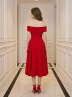 Back view of a woman wearing a red off-the-shoulder midi dress with flared skirt and red heels, standing in a hallway.