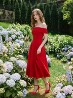 Woman wearing a red off-the-shoulder midi dress with flared skirt and red heels, standing in a garden with hydrangeas.