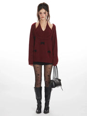Woman wearing a burgundy layered sweater with black bows, black star-patterned tights, and black boots, holding a black handbag.