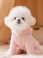 Fluffy white dog wearing a pink gingham dog coat with a hood and a pink pom-pom on the back.