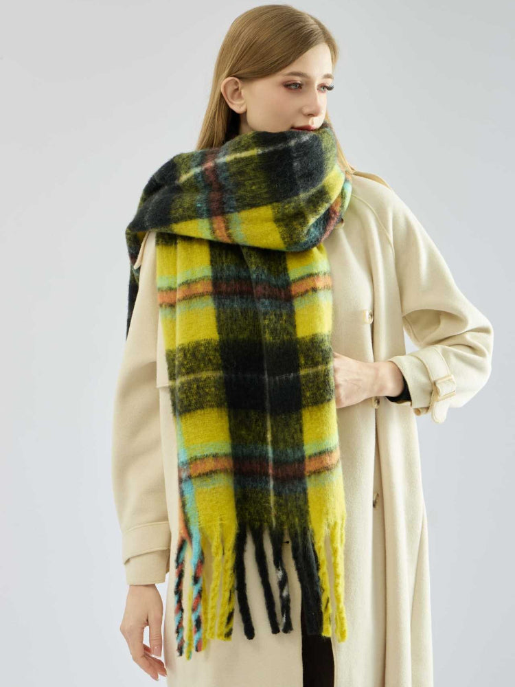 Full body shot of a woman wearing a cream coat and a yellow and black plaid scarf.