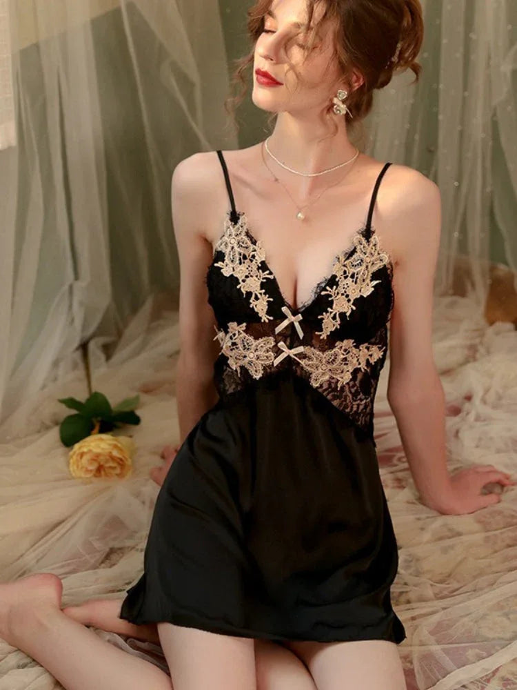 Woman in a black satin slip dress with gold lace detailing, seated on a bed with a yellow rose.