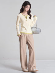 Full-body shot of a woman wearing a cream long-sleeved shirt with green trim and buttons, khaki pants, and holding a silver handbag.