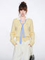 Woman wearing a yellow knit cardigan with a blue and white striped tie and white collared shirt.