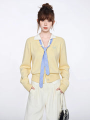 Woman wearing a yellow knit cardigan with a blue and white striped tie and white collared shirt.
