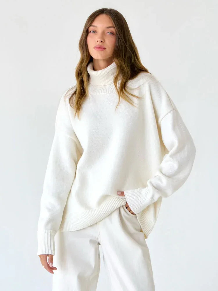 Model wearing an oversized white turtleneck sweater with matching white pants, standing against a white background.