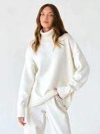 Model wearing an oversized white turtleneck sweater with matching white pants, standing against a white background.