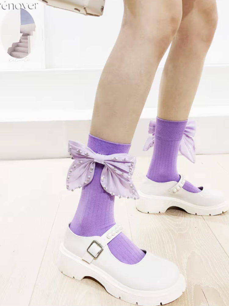 View of purple knee-high socks with decorative bows and pearl accents, paired with white platform shoes.