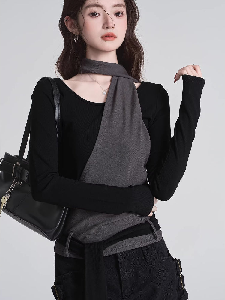 Close-up of a woman wearing a black long-sleeved top with a grey asymmetrical overlay and scarf detail, holding a black handbag.