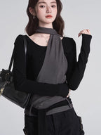 Close-up of a woman wearing a black long-sleeved top with a grey asymmetrical overlay and scarf detail, holding a black handbag.