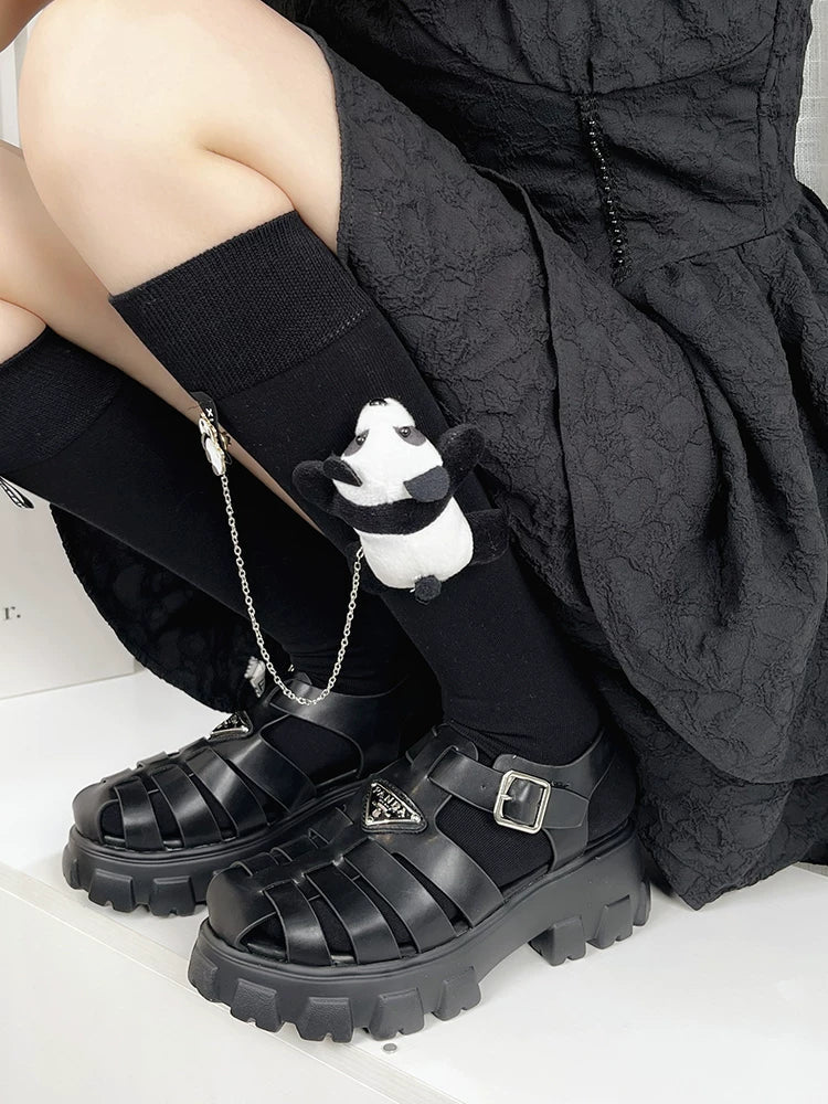 Person wearing knee-high black socks with panda charms and chunky platform sandals