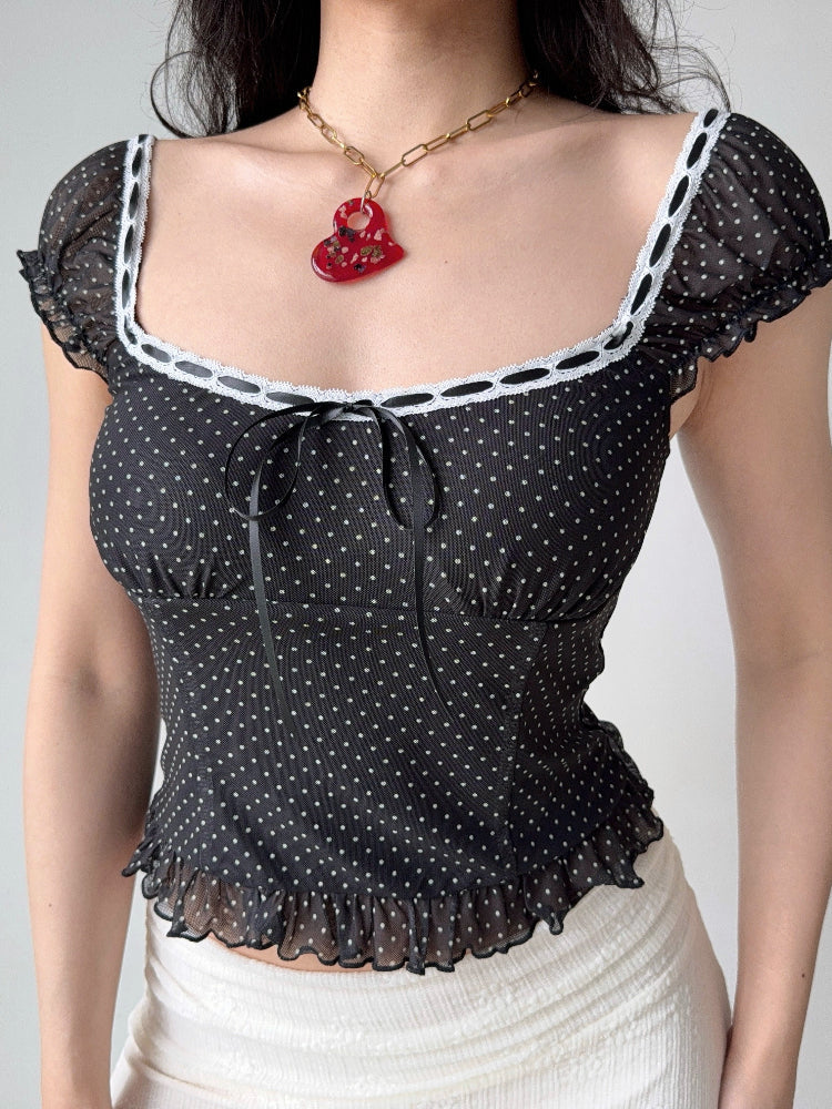 Close-up of a black and white polka dot mesh top with a square neckline and ruffled hem.