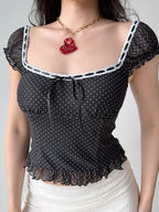 Close-up of a black and white polka dot mesh top with a square neckline and ruffled hem.