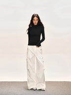 Full body shot of a woman in a black long-sleeve turtleneck top and white cargo pants.