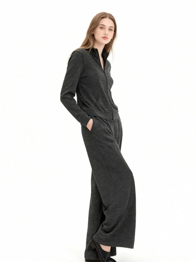 Model wearing a charcoal grey knit zip-up jacket and matching wide-leg pants, side view with hands in pockets.