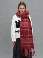Front view of a woman modeling a white graphic sweater and a voluminous red plaid scarf.