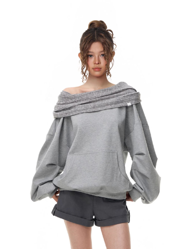 Model wearing a grey off-the-shoulder sweatshirt with a ribbed neckline and voluminous sleeves, paired with grey shorts.