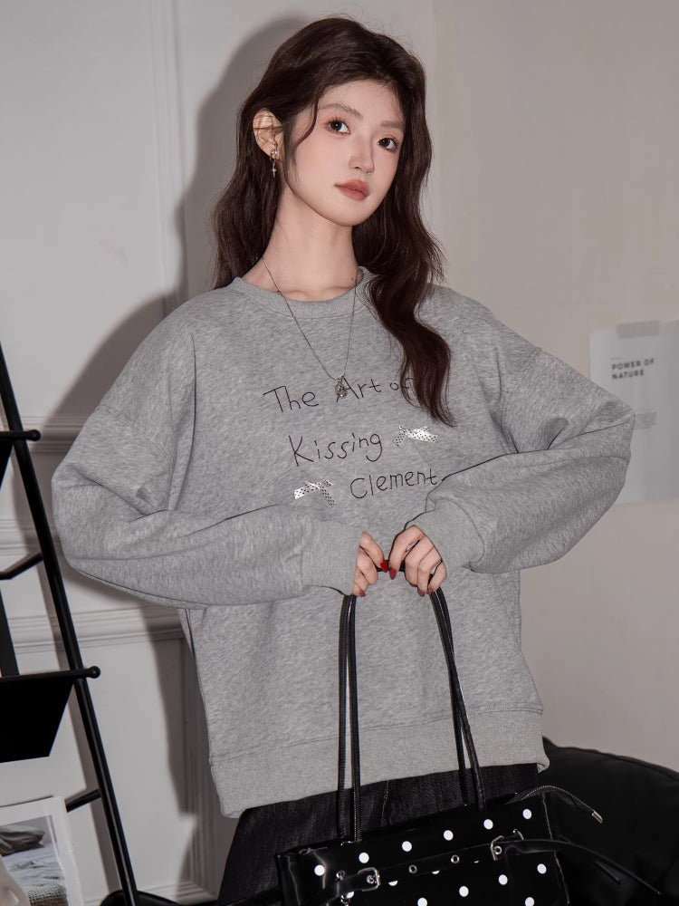 Woman in a grey sweatshirt with graphic print, holding a black handbag