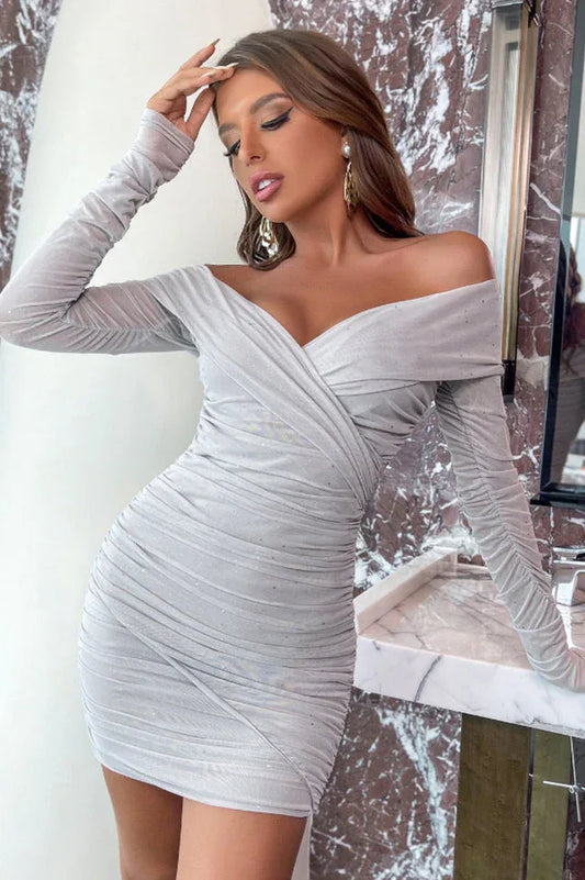 woman wearing a silver off-the-shoulder ruched dress with long sleeves and sparkly embellishments