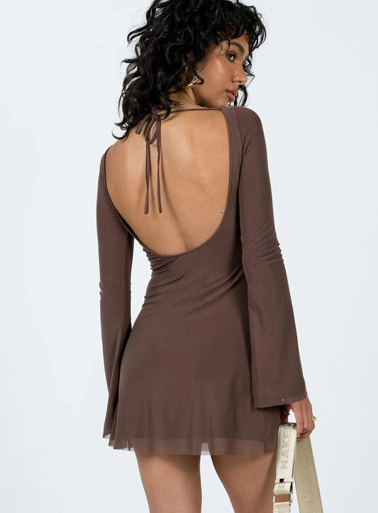 Woman wearing a long sleeve brown mini dress with a boat neckline and a white crossbody bag, back view showing an open back with tie detail.