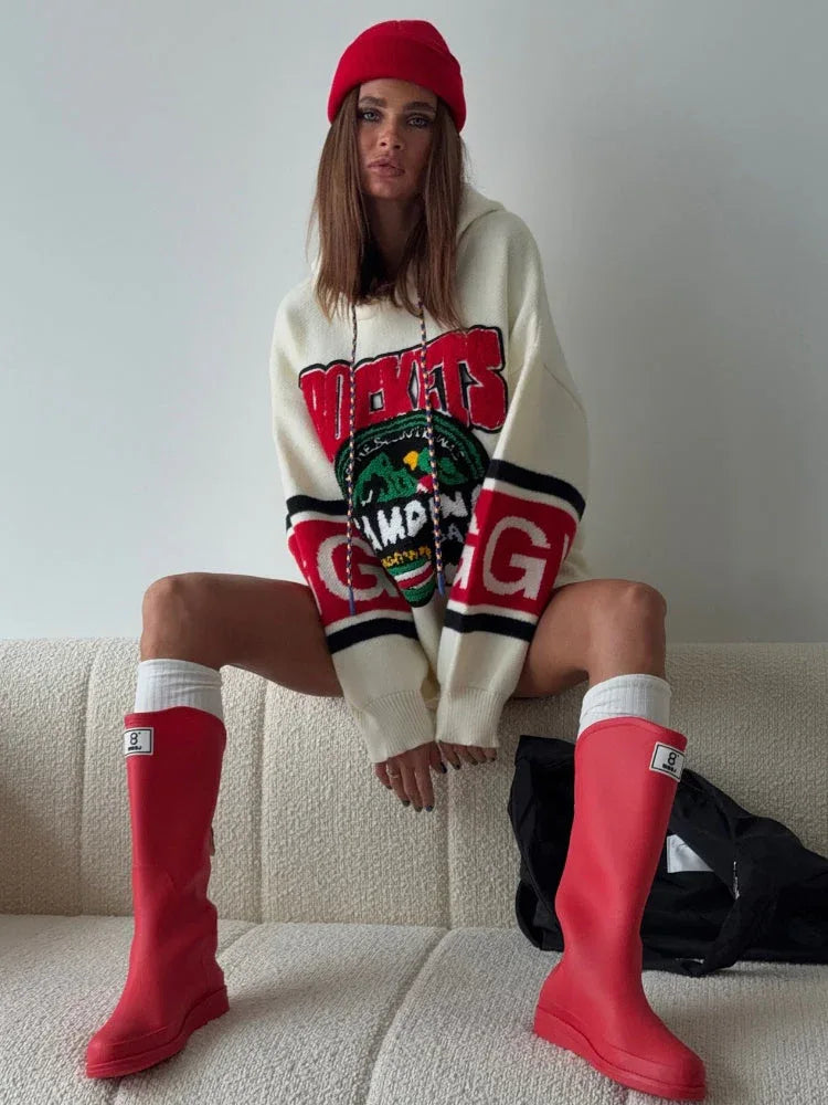 Woman wearing an oversized cream knit hoodie with a red beanie and red boots, sitting on a couch