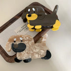 Two dachshund hair claw clips, one brown and yellow, the other beige and black, on a wooden tray