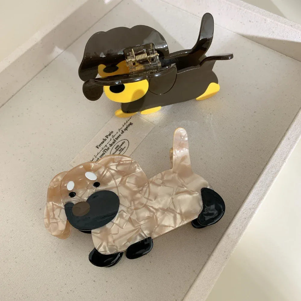 Top view of two dachshund hair claw clips, one brown and yellow, the other beige and black, in a tray
