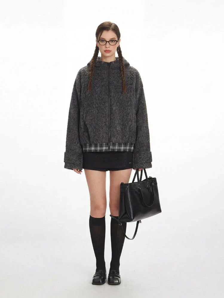 Model wearing a gray fuzzy bomber jacket with a plaid hem, black mini skirt, black knee-high socks, and black loafers, holding a black handbag.