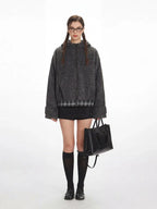 Model wearing a gray fuzzy bomber jacket with a plaid hem, black mini skirt, black knee-high socks, and black loafers, holding a black handbag.