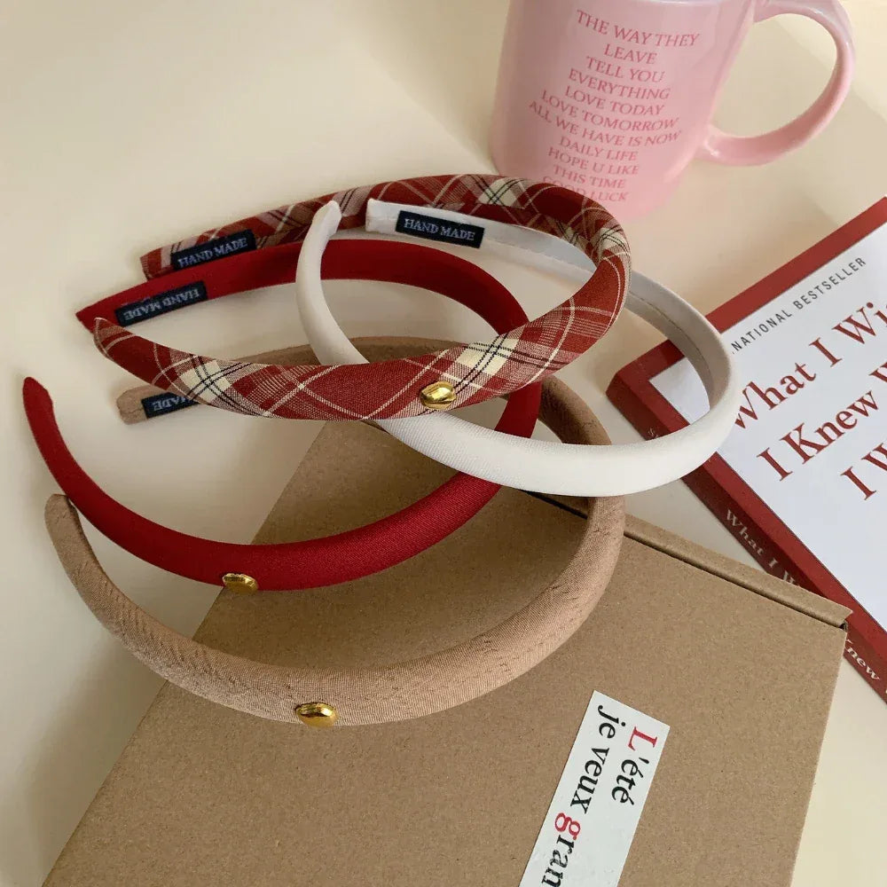 Close-up of padded headbands in red, beige, white, and plaid with a pink mug and book