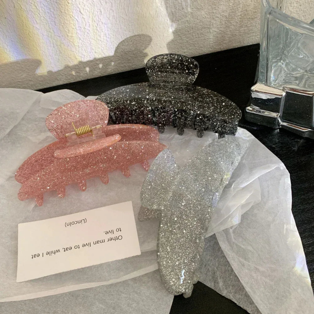 Three glitter claw clips in pink, black, and silver, with the pink clip in the foreground.