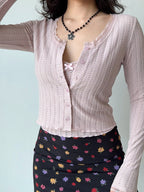 Close-up of a pink cropped knit cardigan with lace trim and a floral print skirt.