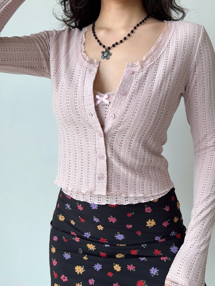 Close-up of a pink cropped knit cardigan with lace trim and a floral print skirt.