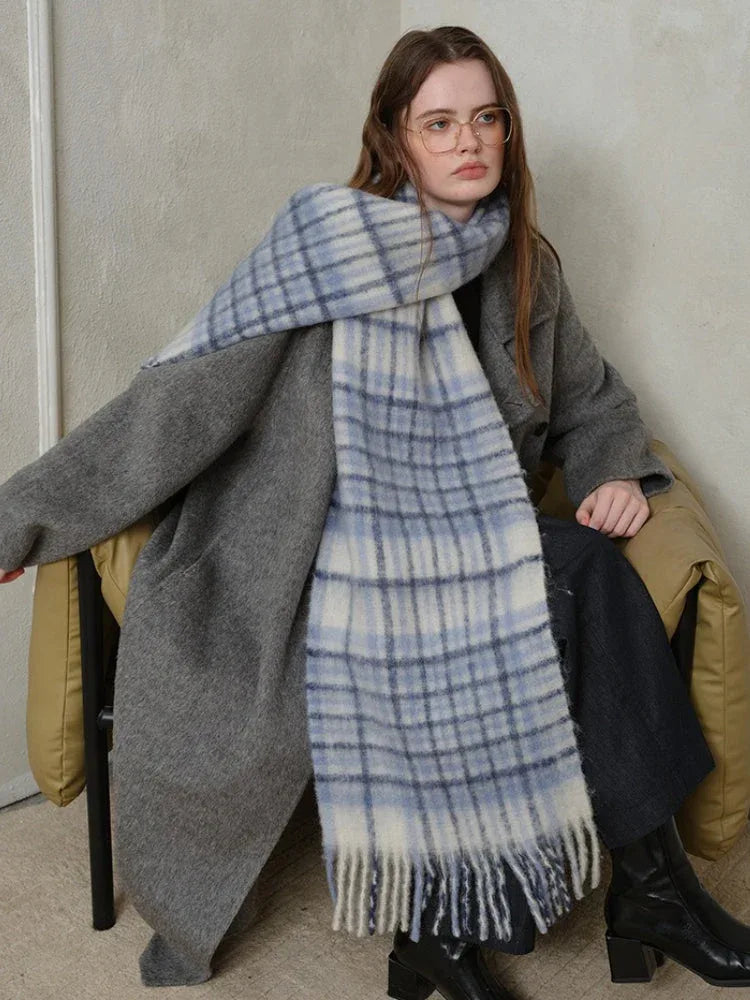 Woman sitting down wearing a grey coat and a blue and white plaid scarf.