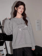 Woman in a grey sweatshirt with graphic print, standing with a handbag