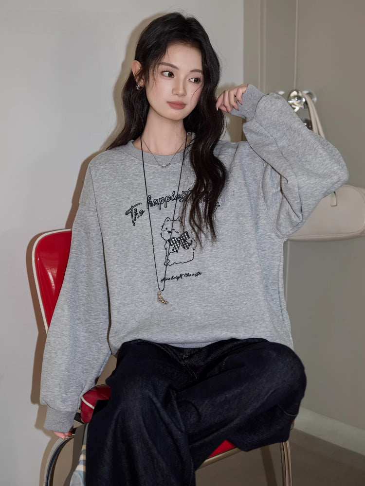 Woman sitting on a red chair wearing a grey crew neck sweatshirt with a graphic print and dark wash jeans