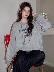 Woman sitting on a red chair wearing a grey crew neck sweatshirt with a graphic print and dark wash jeans
