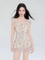 Model wearing a light-colored short dress with a butterfly print and ruffled details.
