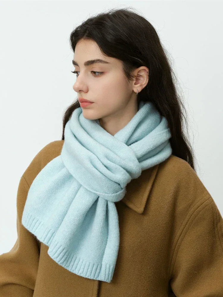 Woman wearing a light blue knitted scarf around her neck and a brown coat.