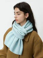 Woman wearing a light blue knitted scarf around her neck and a brown coat.