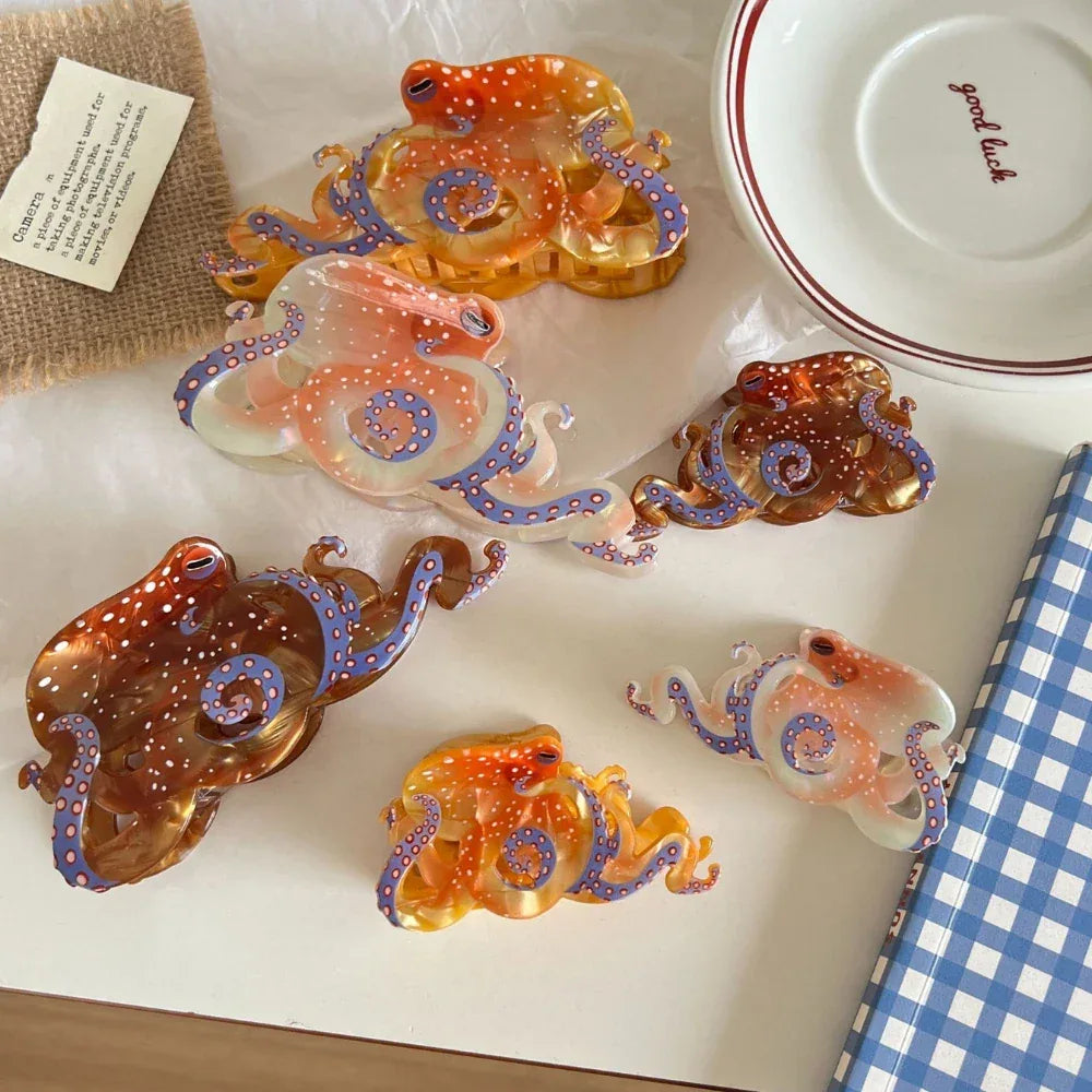 A collection of octopus-shaped hair clips in various translucent colors (orange, brown, pinkish-white) with white polka dots and blue tentacle details, arranged on a white surface with decorative items.
