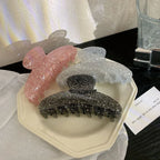 Three glitter claw clips in pink, black, and silver arranged on a white plate, with the black clip in the foreground.