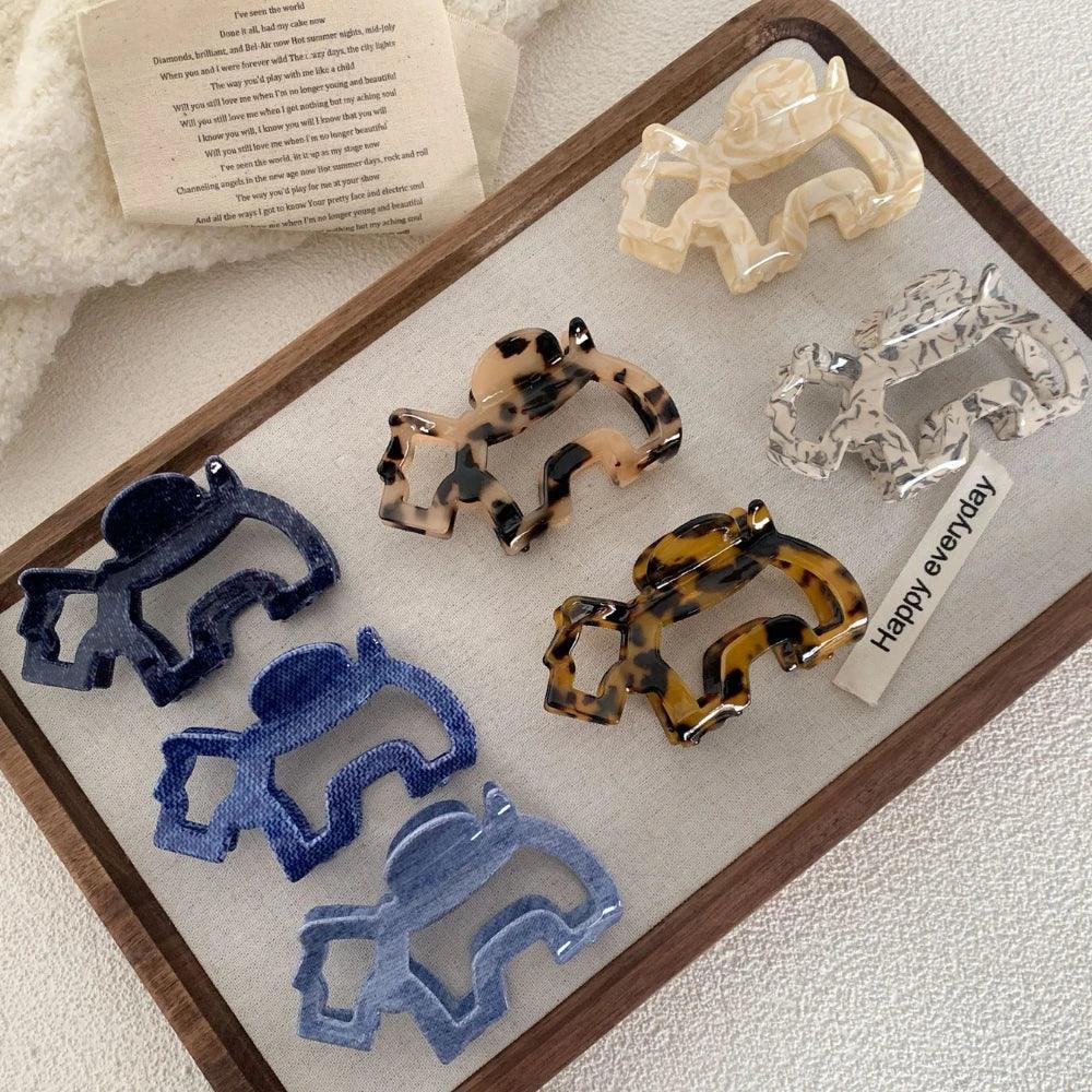 A collection of elephant-shaped hair claw clips in various colors and patterns, arranged on a wooden tray.