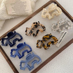 A collection of elephant-shaped hair claw clips in various colors and patterns, arranged on a wooden tray.