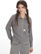 Woman wearing a grey knit zip-up jacket, open at the collar, with a star pendant necklace.